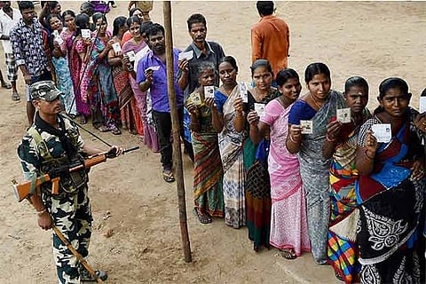 A security person guards as people wait in a queue to cast their votes