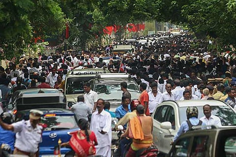 A stream of vehicles, two-wheelers and four-wheelers, and pedestrians stranded on a road