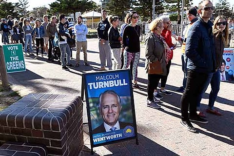 People queue past an election placard outside a voting station in the Sydney