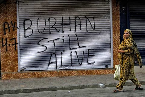 A woman walks past a closed shop painted with graffiti during a curfew in Srinagar