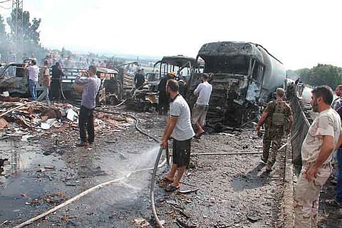 Syrian army soldiers and civilians inspect the site of two explosions that hit the Arzouna bridge
