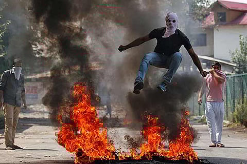 A man in a balaclava jumps over burning debris during a protest in Kashmir