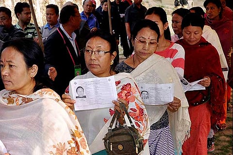 Voters standing in queue show their identity cards