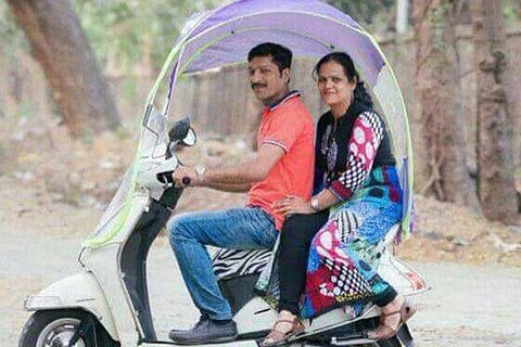A couple travelling on a two-wheeler fitted with an umbrella