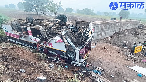 A luxury bus overturned on the side of the road next to a bridge.