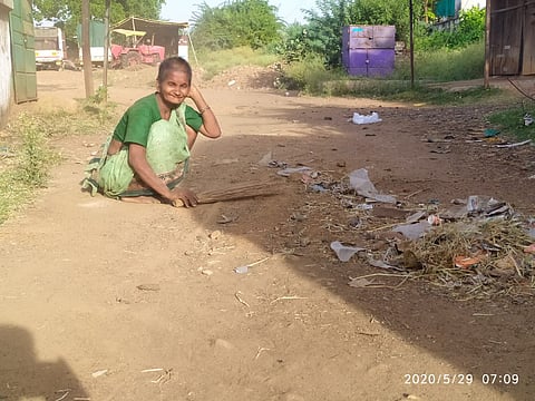 An old woman cleans the streets with a broom in hand