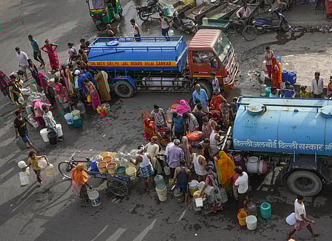 People wait to collect drinking water from a tanker of Delhi Jal Board on a hot summer day as water crisis continues, at a slum in Geeta Colony area