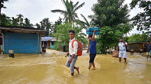 People carry their belongings as they walk through a flooded road following rains after the landfall of cyclone 'Remal', in Nagaon district of Assam
