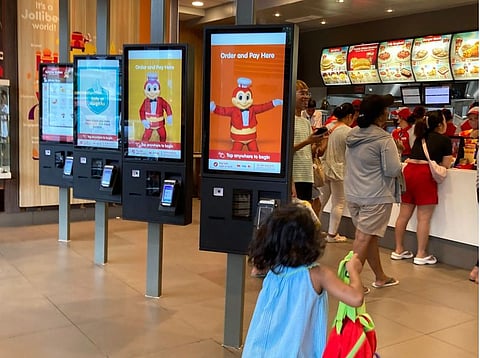 A child next to touchscreen quick-order kiosks inside a Jollibee store in the Philippines.