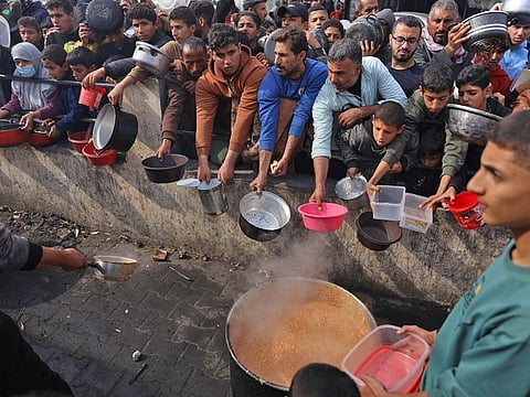 Palestinians hold containers to collect free food handouts from a volunteer hospice in Rafah, southern Gaza.