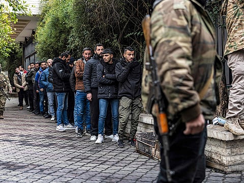 A member of Syria's transitional government security forces stands guard as former soldiers, police members, and civilians queue up at a centre for handing over small arms and security registration with the new authorities in Damascus on December 24, 2024.