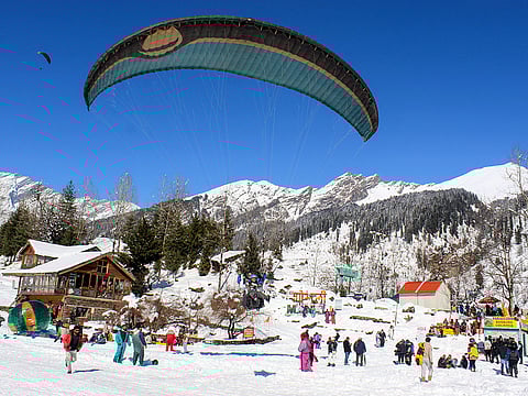 Tourists enjoy paragliding on mountains covered in a thick layer of snow on a sunny day, in Manali on Sunday.