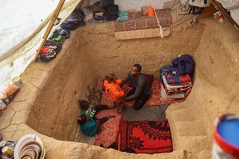 Palestinian father Tayseer Obaid who was displaced with his family from the north of the besieged Gaza Strip, sits with his children in a trench he dug in his tent in an attempt to protect them from the cold and Israeli strikes, in a makeshift camp in Deir Al Balah on January 8, 2025.