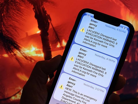 This illustration photo taken January 10, 2025 in Los Angeles, shows the recall message of an evacuation warning issued by the LA County Office of Emergency Management on the screen of a mobile phone in front of a screen showing a photo of the Eaton Fire.