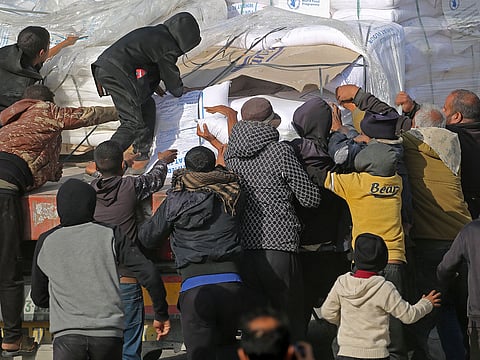 People gather to collect humanitarian aid after trucks arrived in the Gaza Strip via the Kerem Shalom crossing, also known as Karem Abu Salem, on January 19, 2025.