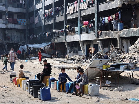 Palestinian children sit and wait next to water cans at a school turned shelter in Jabalia in the northern Gaza Strip on February 4, 2025.