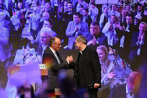 Leader of Germany's Christian Democratic Union (CDU) Friedrich Merz (L) and Bavaria's State Premier and Leader of the conservative Christian Social Union (CSU) Markus Soeder (R) shake hands in front of cheering supporters during the final campaign event of Germany's Christian Democratic Union party on the eve of general elections in Munich.