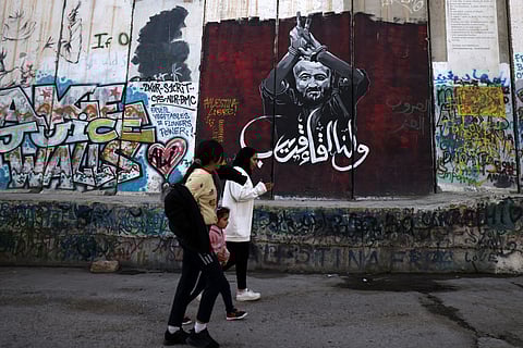 Palestinian youths walk along the separation wall between Israel and the occupied West Bank, past a mural painting depicting jailed Palestinian politician Marwan Barghouty, in Bethlehem on February 26, 2025.