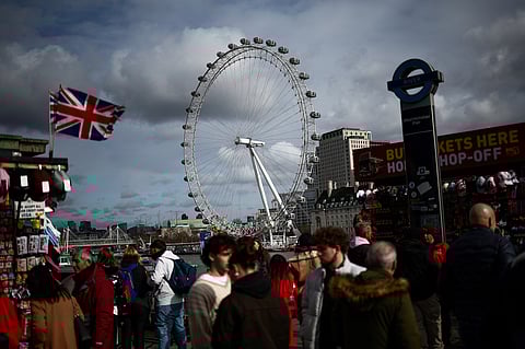 Pedestrians walk along Embankment backdropped by The London Eye, in London.