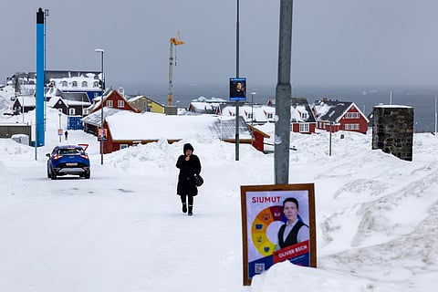 A political poster sits at the side of the road as a woman walks in the snow, in Nuuk, Greenland, on March 8, 2025.