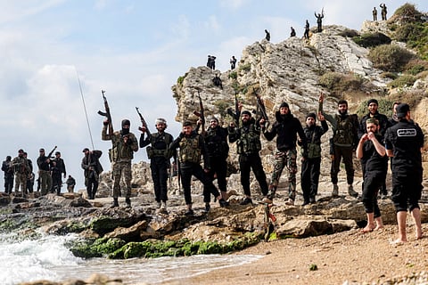 Members of security forces loyal to the interim Syrian government pose together with their firearms as they stand along a rocky beach by the Mediterranean sea coast in Syria on March 9, 2025.