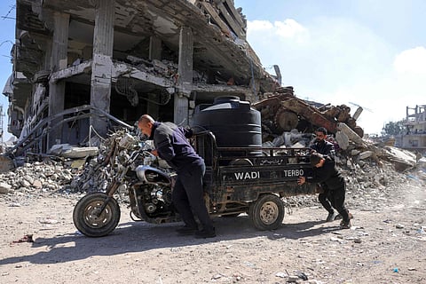Palestinians push a vehicle carrying a water tank past destroyed buildings at a displacement camp west of Jabalia city in the northern Gaza Strip on March 11, 2025.