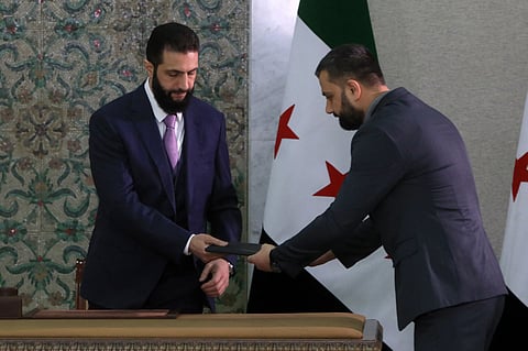 Syria's interim President Ahmad Al Sharaa receives the country's constitutional declaration, which will be enforced throughout a five-year transitional period, before signing it at the presidential palace in Damascus on March 13, 2025.