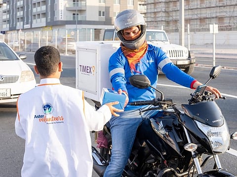 An Aster volunteer handing over a food box to a motorcyclist at a traffic junction in Dubai.