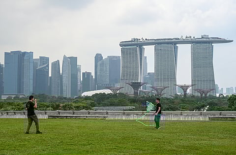People fly a kite on the rooftop of Marina Barrage with a backdrop of the city skyline blanketed in haze amidst moderate levels of air pollution in Singapore on March 26, 2025.