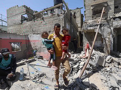 A Palestinian man carries children across the rubble of a house that was destroyed in an Israeli airstrike in Khan Yunis in the southern Gaza Strip on March 31, 2025.