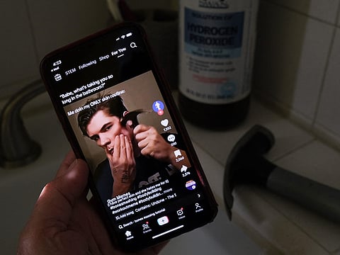 This illustration photo shows a video of male TikTok influencer hammering his cheekbone, playing on a smartphone in a bathroom next to a bottle of hydrogen peroxide and a hammer in Los Angeles, April 11, 2025.