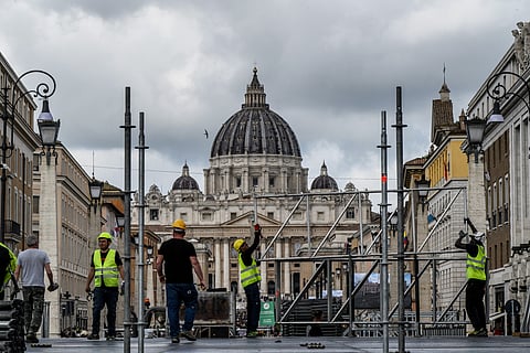 Workers build a tribune with the St Peter's Basilica of the Vatican in the background, on Via della Conciliazione street in Rome on April 25, 2025.