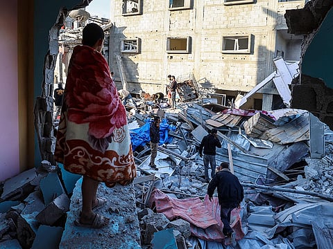 A youth draped in a blanket looks on as people look for survivors in the rubble of a building hit in an Israeli strike in the Bureij camp for Palestinian refugees in the central Gaza Strip on May 2, 2025.