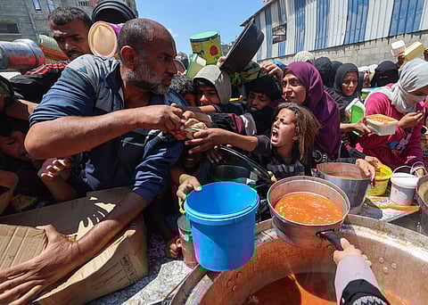 Displaced Palestinians snatch bread loaves distributed by a charity kitchen at the Nuseirat refugee camp in the central Gaza Strip on May 5, 2025.