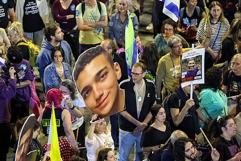 A demonstrator holds a sign showing the face of Israeli-US hostage Edan Alexander (C) during a protest calling for action to release the remaining hostages held captive in Gaza since the 2023 October 7 attacks by Palestinian militants, outside the Israeli Defence Ministry headquarters in Tel Aviv.