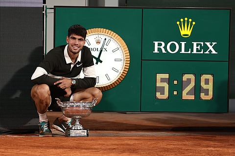 Spain's Carlos Alcaraz poses the trophy next to the clock that shows the duration of the match, the longest for a final in Roland-Garros, after winning against Italy's Jannik Sinner at the end of their men's singles final match on day 15 of the French Open tennis tournament on Court Philippe-Chatrier at the Roland-Garros Complex in Paris on June 8.