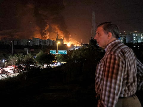 A man watches near a blocked highway with traffic as a fire blazes in the oil depots of Shahran, northwest of Tehran, on June 15, 2025.