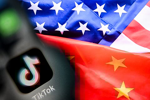 A photo taken on April 10, 2025 shows the Chinese social networking service TikTok's logo on a smartphone screen (L) and US' and China flags combo illustration on a laptop screen in Frankfurt am Main, western Germany.