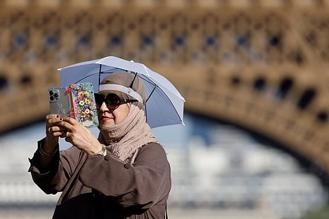 A tourist uses a small umbrella hat to protect herself from the sun during a heatwave at the Trocadero square near the Eiffel Tower, in Paris, on June 30, 2025.
