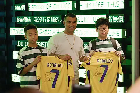 This frame grab from AFPTV video footage shows two fans receiving autographed Cristiano Ronaldo jerseys while posing with the footballer's brother Hugo dos Santos Aveiro (C) during the opening of the CR7 LIFE Museum in Hong Kong on July 7, 2025.