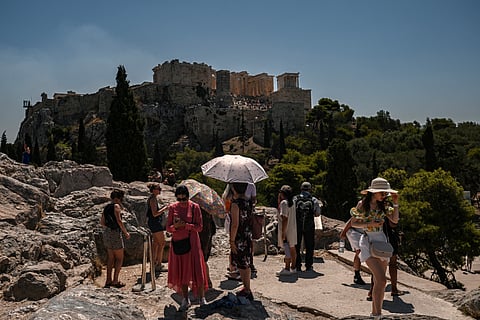 Tourists some holding umbrellas, gather opposite Acropolis Hill in Athens on July 8, 2025.