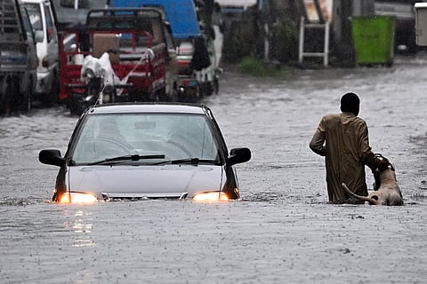 A man along with his dog while a car wade through a flooded street during heavy monsoon rains in Rawalpindi on July 17, 2025.