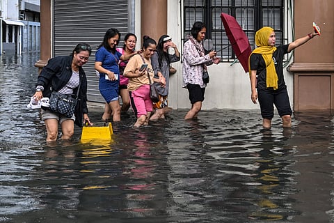 A woman poses for a selfie while wading with others through a flooded street in Manila on July 22, 2025, after heavy rains caused floodings enhanced by monsoon.