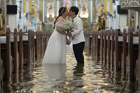 Newlyweds Jade Rick Verdillo right, and Jamaica kiss during their wedding at the flooded Barasoain church in Malolos, Bulacan province, Philippines on Tuesday, July 22, 2025.