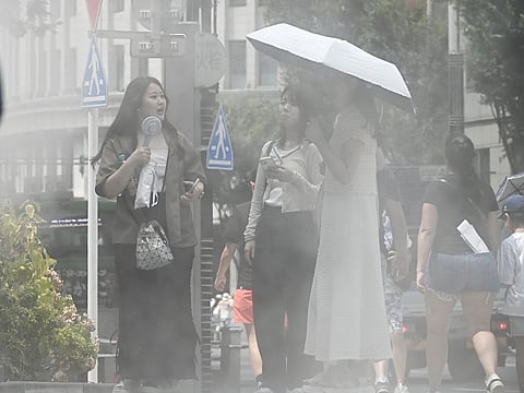 Pedestrians cool off under a water mist spray in Ginza district during high temperatures in Tokyo, Japan, on Wednesday, August 6, 2025.