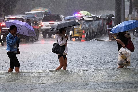 People wade through a flooded street in Manila on July 22, 2025, after heavy rains caused floodings enhanced by monsoon.