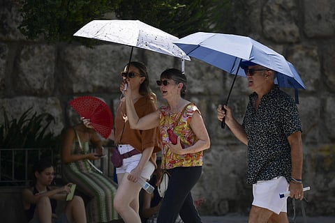 People protect themselves from the sun with an umbrella during the extreme heatwave in Seville, Spain, that exceeds forty degrees, in Seville on August 12, 2025.  The satellite  will monitor ocean and land temperatures, water vapour and greenhouse gases in the atmosphere, the amount of desert dust and cloud cover.