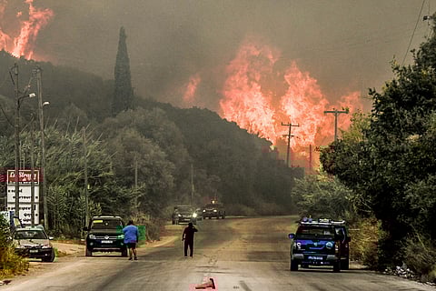 Inhabitants stand on a road as a wildfire burns a forest near the city of Patras, western Greece on August 12, 2025.