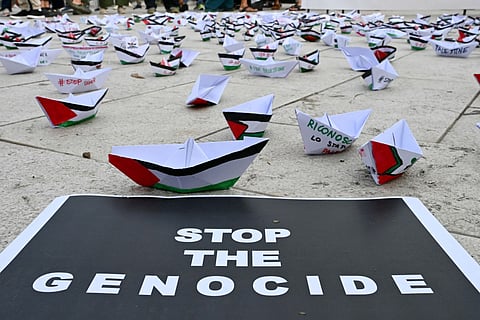 A flotilla of paper boats are laid on the ground near a poster reading "Stop the Genocide" during a demonstration in support of Gaza and Palestinian people at Venice Lido during the 82nd Venice International Film Festival, on August 30, 2025.