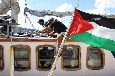 Pro-Palestinian activists work on a vessel of a civilian flotilla, carrying humanitarian aid and aiming to break the Israeli blockade of the Gaza Strip, as it remains moored at Barcelona port on September 1, 2025, after being forced to return due to bad weather.